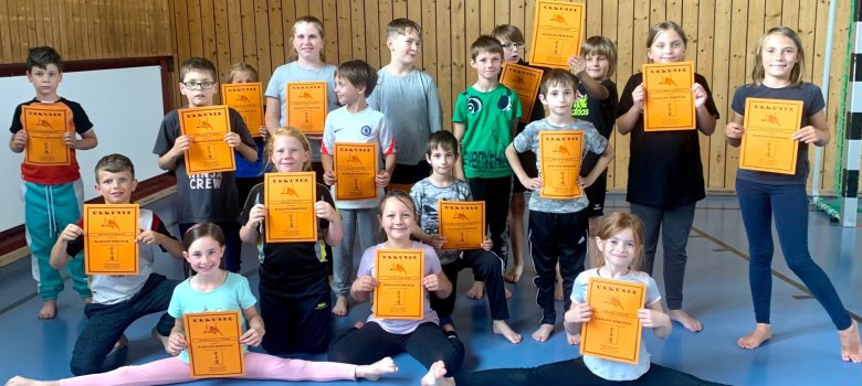 The photo shows a group picture of the participants with their certificates. In the foreground are two girls doing the splits.