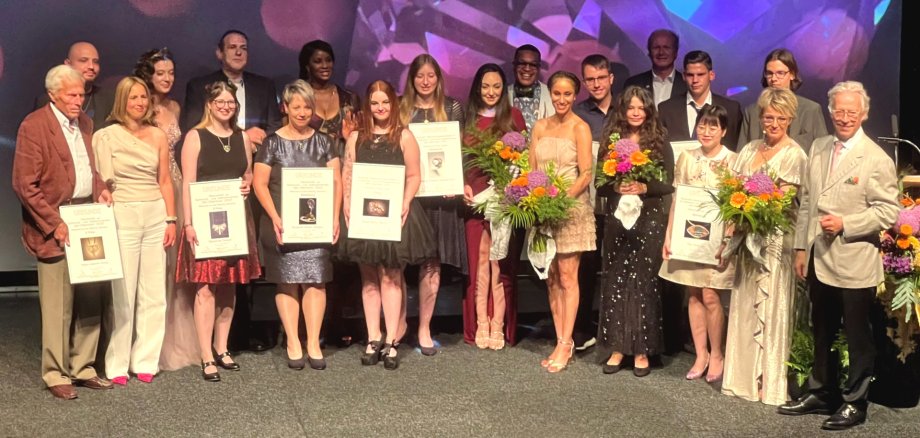 The photo shows many people on the stage of the Stadttheater: the organizers, the presenter, the artists and the award winners with their certificates,