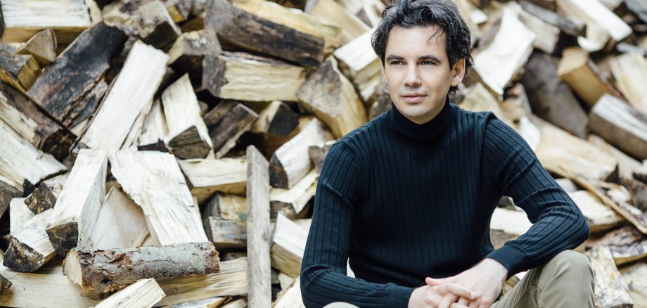 The photo shows Martin Stadtfeld in front of a pile of wood.