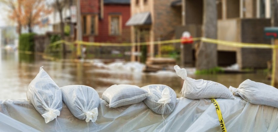The photo shows a row of sandbags in front of a flooded house front.