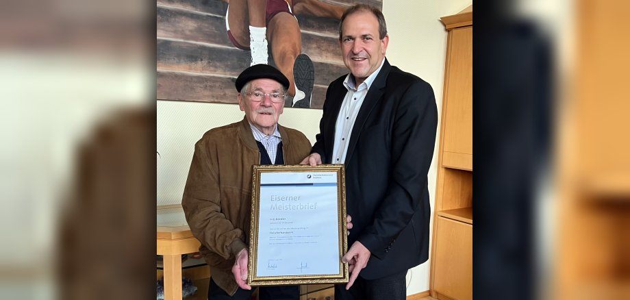 The photo shows Fritz Börstler and Lord Mayor Frank Frühauf. They stand next to each other in the Lord Mayor's office and hold the Iron Master Craftsman's Certificate up to the camera.