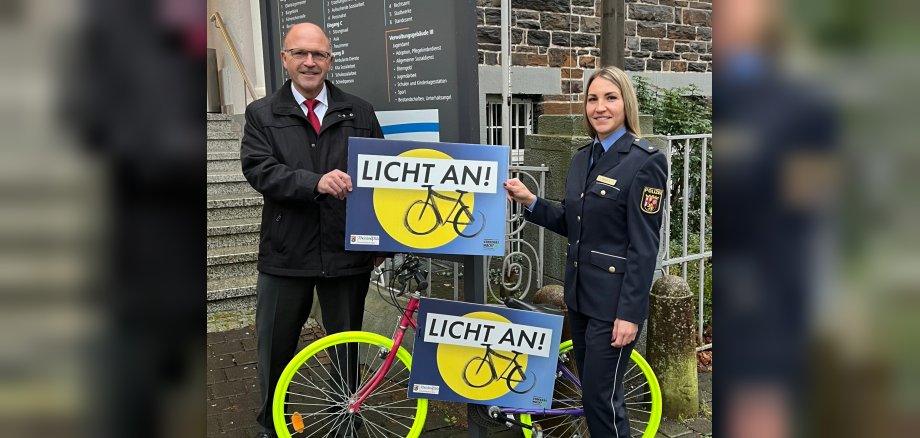 The photo shows Mayor Marx and Police Councillor Short. They are standing in front of the town hall with one of the spray-painted bikes and holding a sign with the words "Lights on!"