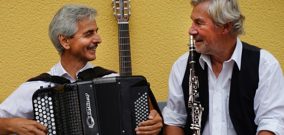 The photo shows the two musicians. They are sitting on a bench and looking at each other. Victor Pribylov is holding an accordion, Uli Holzhausen a clarinet.