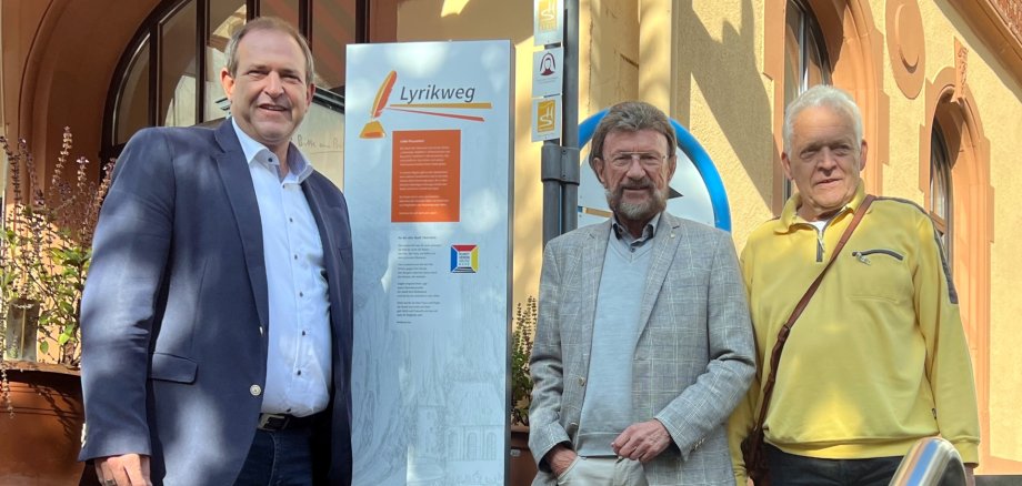 The photo shows the people mentioned. Mayor Frühauf is standing to the left of the signpost for the poetry trail at the entrance to the Felsenkriche. Wolfgang Hey and Joachim Schroetter to the right.