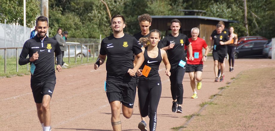 The photo shows nine athletes running one after the other on a track.