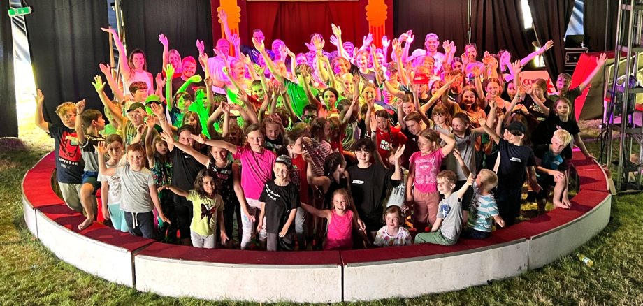 The photo shows a group picture of the children, supervisors and visitors in the circus ring.