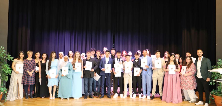 The photo shows the students receiving their certificates on the stage of the Göttenbach auditorium.