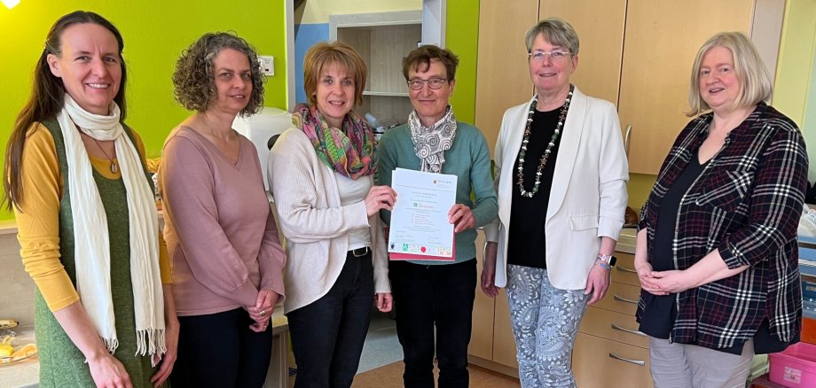 The picture shows the project participants being presented with the certificate by Irmgard Lüttiken to daycare center director Silke Fritsch. Silke Fritsch (3rd from left) is delighted with her. They were joined by Tina Weber, Anja Pullem, Katrin Schwarz and daycare center consultant Juliane Groß.