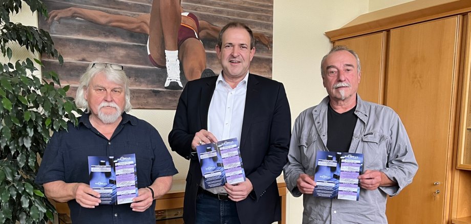 The photo shows the aforementioned people standing next to each other in Mayor Frühauf's office. They are holding flyers with the concert program in their hands and looking into the camera.