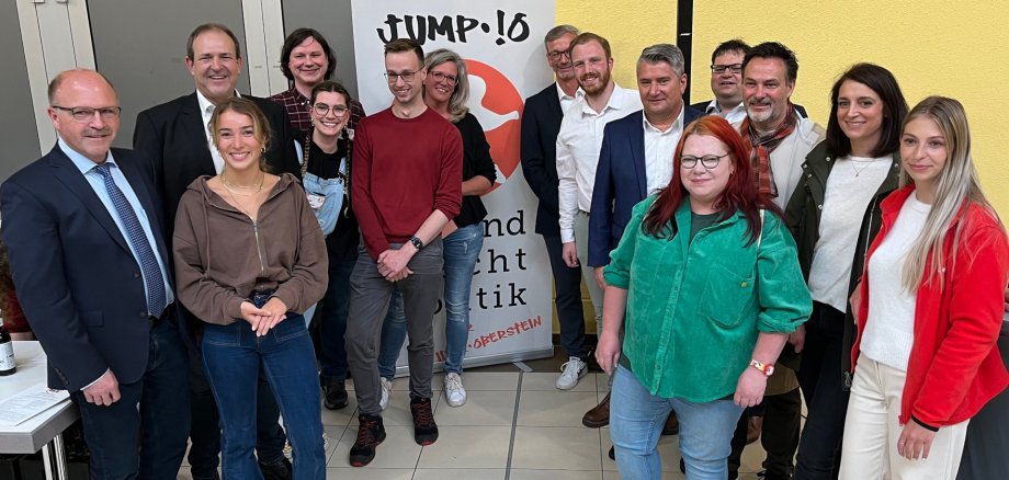 The photo shows 15 people standing in front of a roll-up of the Jump-!O project at the Idar-Oberstein trade fair and looking into the camera.