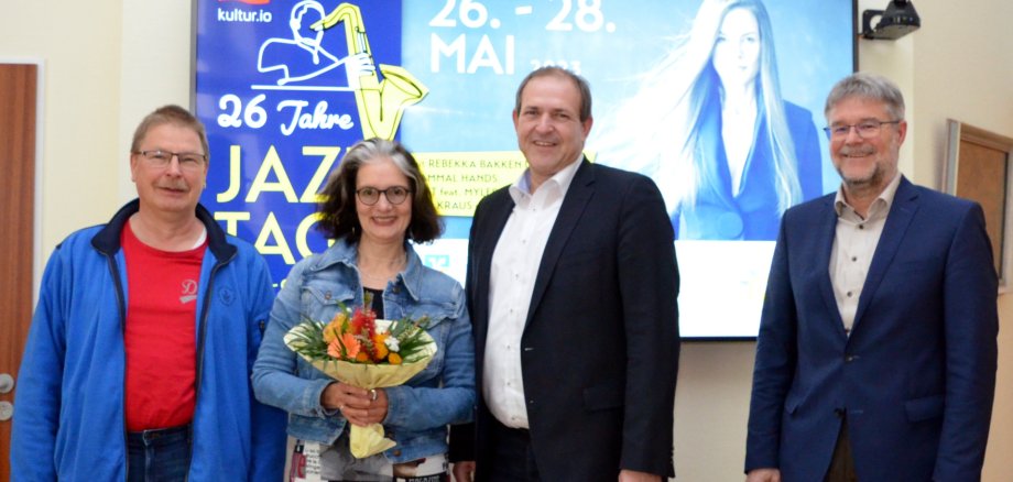 La photo montre de gauche à droite le représentant du comité du personnel Volker Poes, la conseillère culturelle Annette Strohm, le maire Frank Frühauf et le chef de bureau Wolfgang Petry devant une affiche des Jazztage Idar-Oberstein 2023.