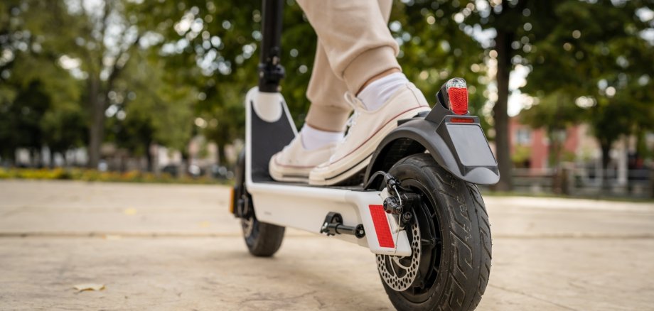 La photo montre les pieds d'une personne debout sur un scooter électrique.
