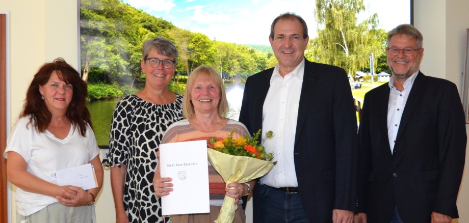 La photo montre les personnes mentionnées dans l'article, Monika Gross avec un certificat et un bouquet de fleurs.