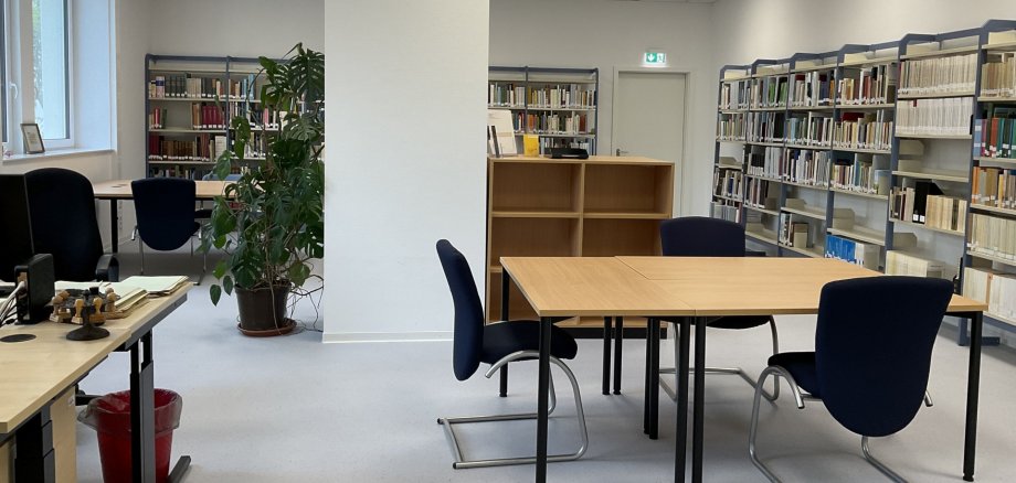 La photo montre la salle de lecture des archives municipales avec des tables, des chaises et des étagères.