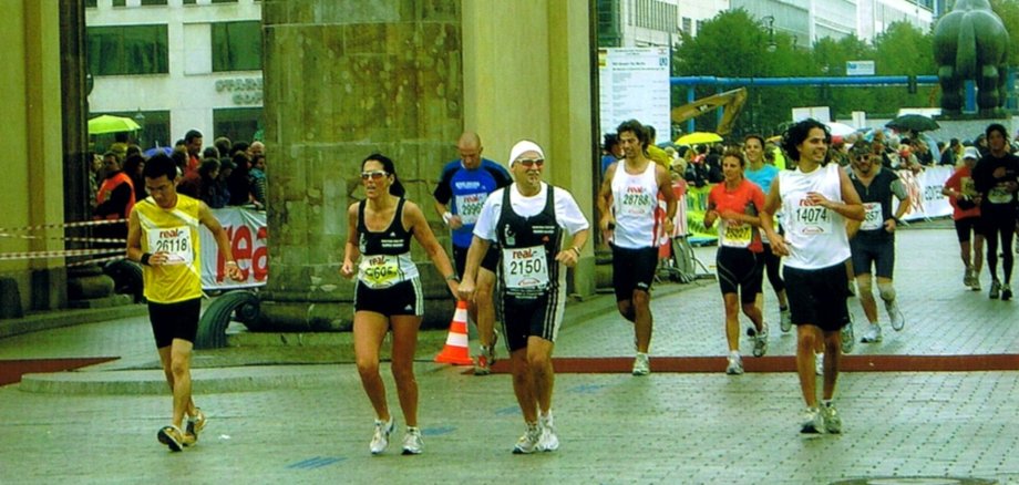 La photo montre plusieurs coureurs franchissant la ligne d'arrivée du marathon de Berlin à la porte de Brandebourg. Au centre, Ilonka et Rainer Hagner franchissent la ligne d'arrivée main dans la main.