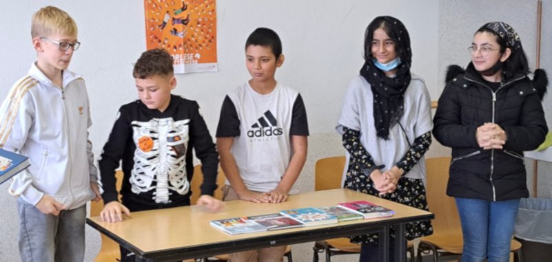 La photo montre les cinq participants au concours de lecture. Ils se tiennent côte à côte derrière une table.