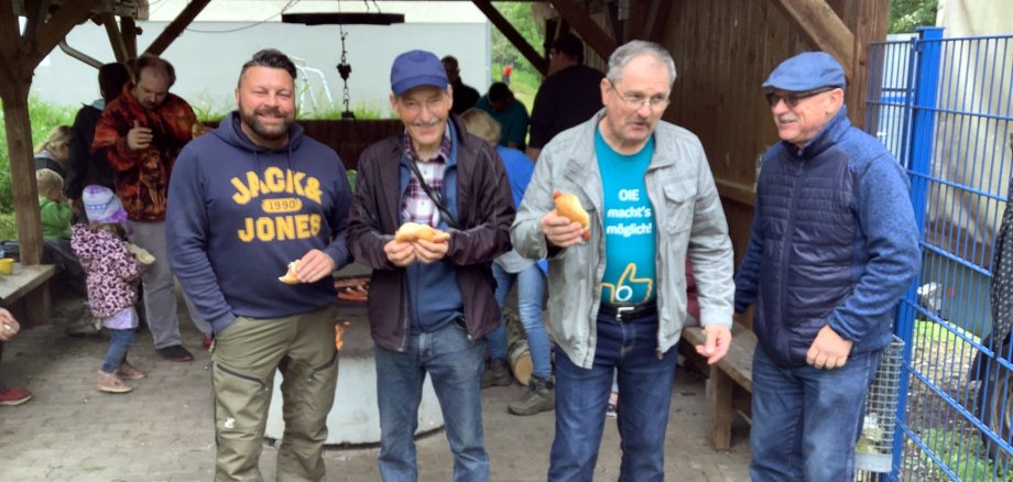La photo montre quatre membres du Groupe Ouvert de Nahbollenbach qui se tiennent devant la grille du barbecue avec des saucisses.