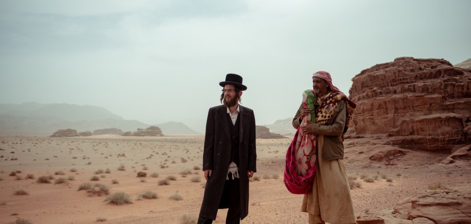 La photo montre deux hommes debout dans un désert. Ils regardent ensemble au loin.