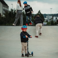 La photo montre un enfant en trottinette sur le skatepark.