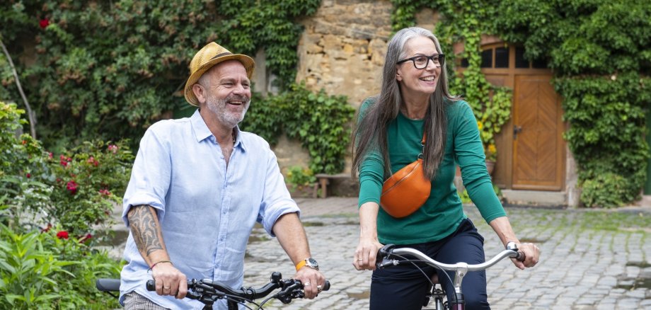 La photo montre un homme et une femme. Ils sont debout dans un parc avec leurs vélos et regardent au loin.