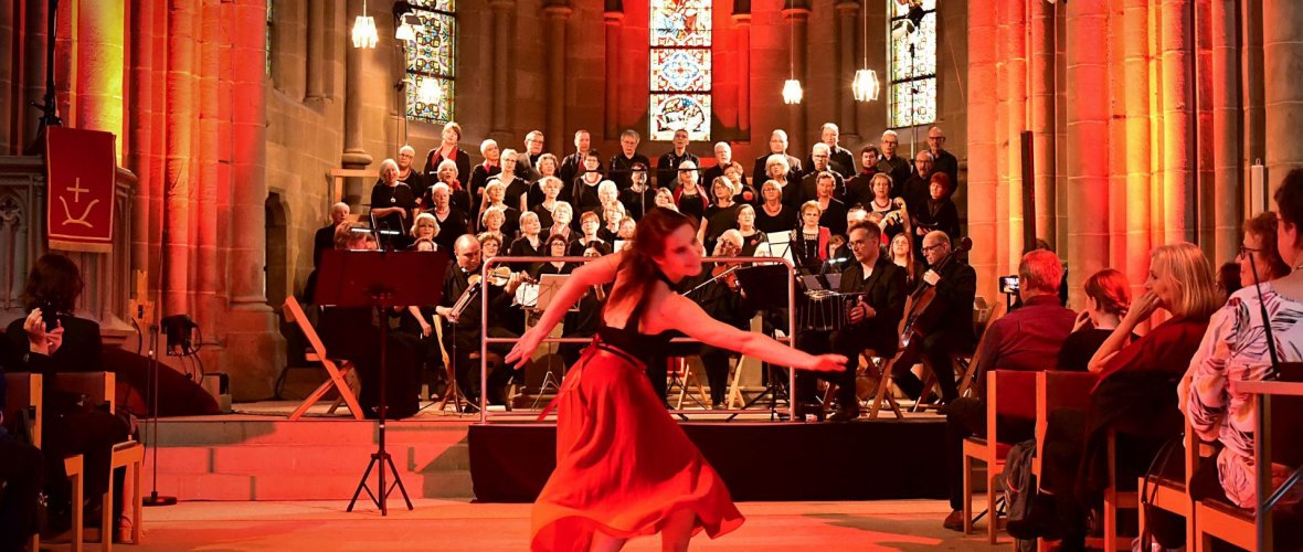 Das Foto zeigt eine Tänzerin in einer Kirche und im Hintergrund ist ein Orchester und ein Chor.