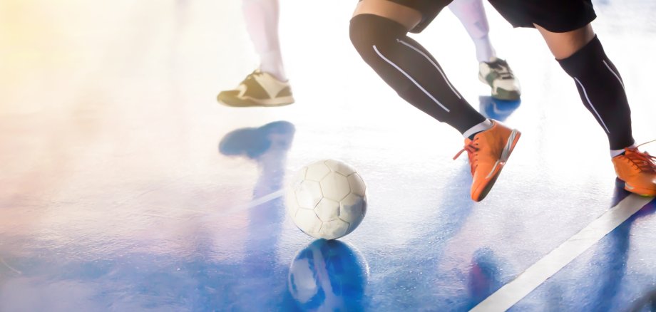 Das Foto zeigt Beine von Fußballern, die in einer Sporthalle spielen.