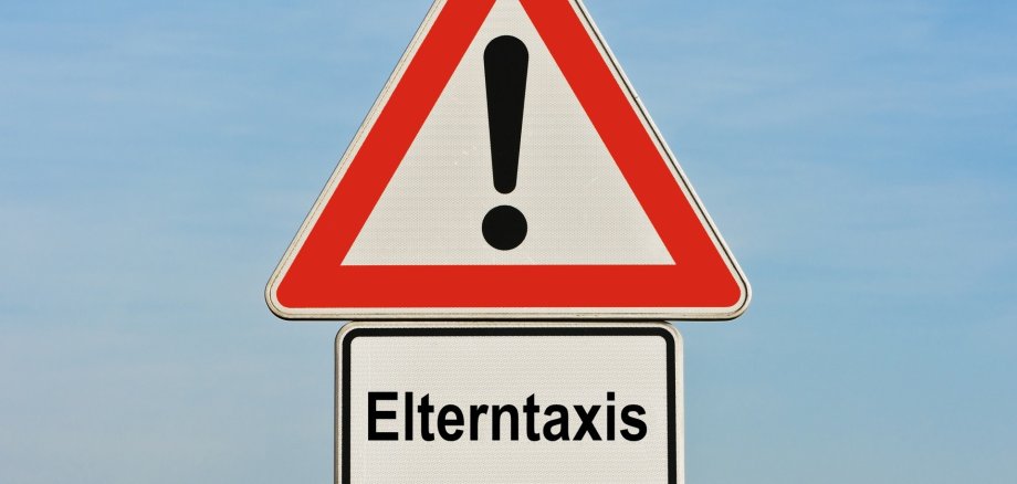 Das Foto zeigt das Verkehrsschild "Achtung Gefahrenstelle" mit Zusatzschild "Elterntaxis"