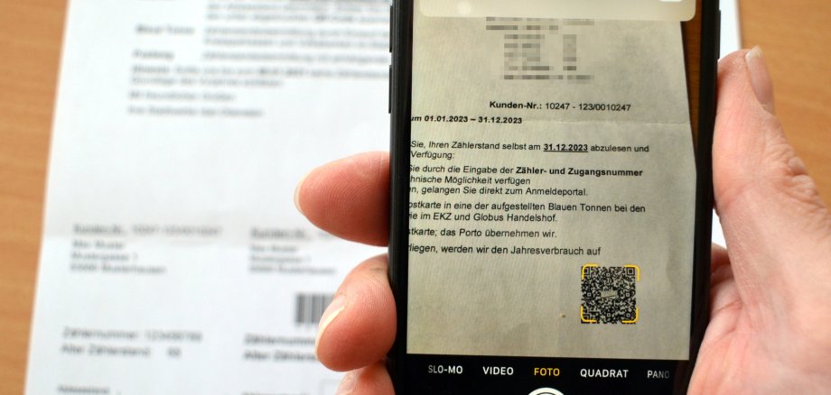 Das Foto zeigt ein Smartphone. Es wird über die Ablesekarte gehalten und scannt den QR-Code, der zur Zählerstandsmeldung auf der städtischen Homepage führt.