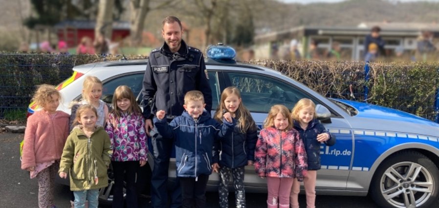 Das Foto zeigt mehrere Kinder, die mit dem Polizisten Pascal Stamm vor einem Polizeiauto stehen.