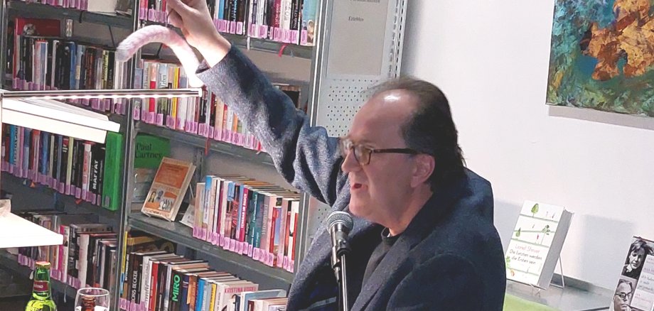Das Foto zeigt den Autor bei der Lesung, er hält einen umhäkelte Kleiderbügel hoch.