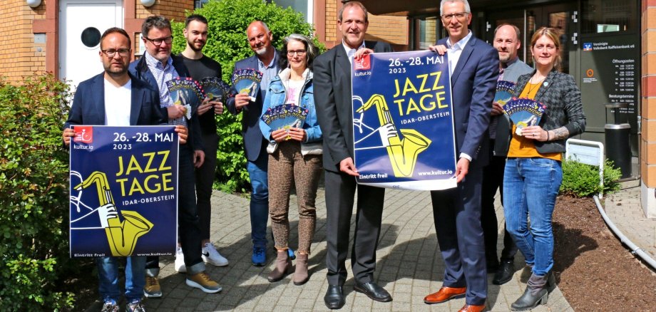 Das Foto zeigt die Vertreter der Stadt und der Sponsoren mit Plakaten und Flyern der Jazztage vor dem Gebäude der Vereinigten Volksbank-Raiffeisenbank.