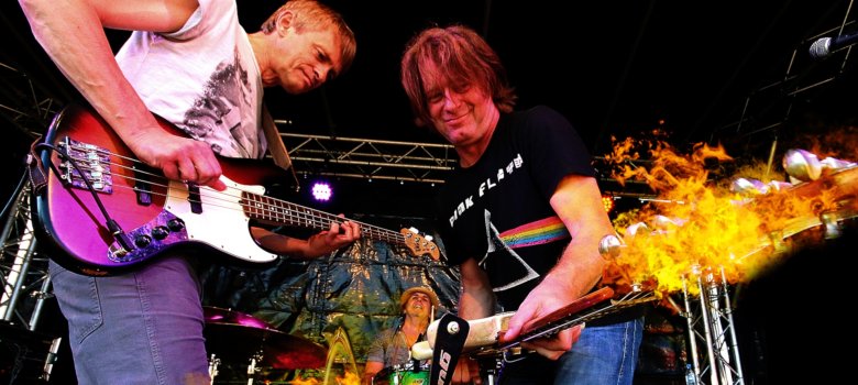 Das Foto zeigt die Gitarristen Thomas Blug und Rudi Spiller auf der Bühne, aus ihren Gitarren schießen Flammen.