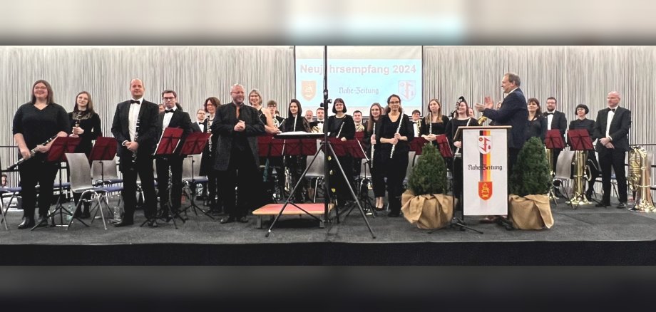 Das Foto zeigt einen Blick auf die Bühne des Neujahrsempfangs. Die Mitglieder des SBO stehen auf der Bühne, Oberbürgermeister Frühauf steht am Rednerpult, hat sich dem Orchester zugewandt und applaudiert.