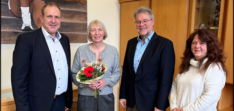 Das Foto zeigt die genannten Personen. Sie stehen nebeneinander im Büro des Oberbürgermeisters. Die Jubilarin hält einen Blumenstrauß in den Händen.