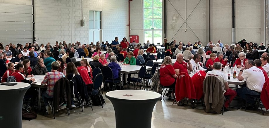 Das Foto zeigt einen Blick in die Messehalle. Zahlreiche Teilnehmer des Ehrenamtsfestes sitzen in Gruppen an Tischen.